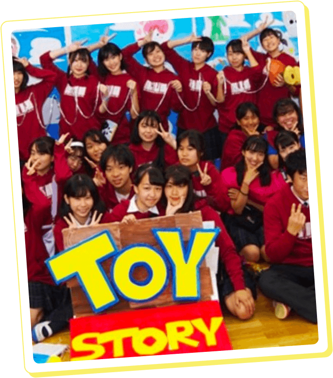 制作事例：赤いトップスを着た生徒たちがトイ・ストーリーのロゴボードを囲んで笑顔でポーズをとる集合写真